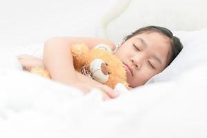 schattig weinig Aziatisch meisje slaap en knuffel teddy beer Aan bed foto