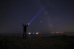 silhouet van Mens met zaklamp stralend straal naar melkachtig manier heelal foto