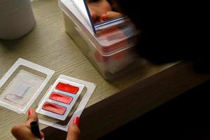 dichtbij omhoog hand- van vrouw toepassen bedenken met kunstmatig, klein borstel Aan houten tafel en haar nagel is roze. foto