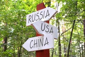 Verenigde Staten van Amerika, Rusland en China - houten wegwijzer met drie pijlen, Woud in achtergrond foto