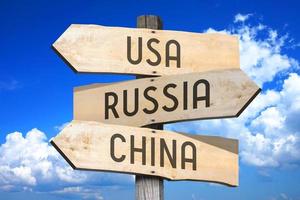 Verenigde Staten van Amerika, Rusland, China - houten wegwijzer met drie pijlen, lucht met wolken in achtergrond foto