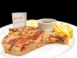 t-bone varkensvlees steak met Frans Patat, ananas plak en peper saus met steak mes en vork Aan wit keramisch bord isoleren Aan zwart achtergrond en maken met paden. foto