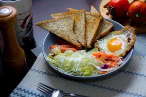 ontbijt, gebakken eieren, gebakken worst, groente salade en geroosterd brood Aan een bruin houten tafel met koffie. foto