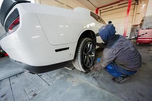 monteur in onderhoud reparatie station werken met spier auto. Mens arbeider aansluitingen omhoog de auto naar diagnostiseren de chassis. foto