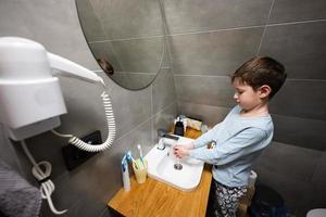 jongen wast handen in de wastafel Bij badkamer. foto