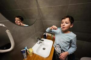 jongen borstel tanden in spiegel Bij badkamer. foto