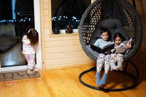 broer met zus lezing boeken in comfortabel hangende stoel in knus houten klein cabine huis. leven in platteland. foto