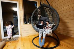 broer met zus lezing boeken in comfortabel hangende stoel in knus houten klein cabine huis. leven in platteland. foto