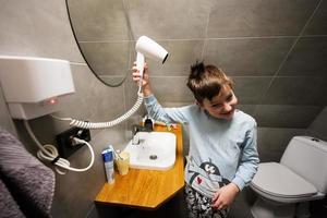 jongen droogt haar- met een haar- droger Bij badkamer. foto