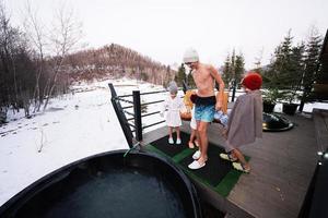 kinderen voorbereidingen treffen het baden in houten vat heet kuip in de terras van de huisje. Scandinavisch bad met een haard naar brandwond hout en warmte water. foto