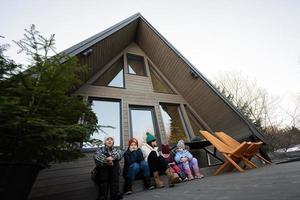 moeder met vier kinderen zitten Aan terras uit rooster klein huis in de bergen. foto