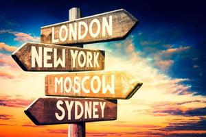 Londen, nieuw york, Moskou, Sydney - houten wegwijzer met vier pijlen, zonsondergang lucht in achtergrond foto