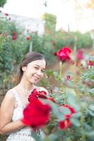 jong Aziatisch vrouw vervelend een wit jurk poses met een roos in roos tuin foto