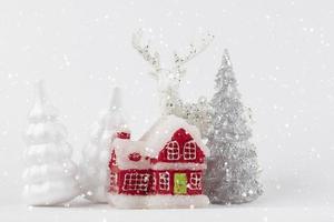 Kerstmis tafereel, miniatuur datsja dorp. Kerstmis weinig rood huizen, hert en besneeuwd Spar bomen Aan een wit achtergrond. feestelijk modern decoraties. foto