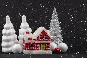 feestelijk besneeuwd donker Kerstmis achtergrond. rood miniatuur huis omringd door wit Kerstmis bomen. foto
