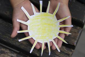de handen van een klein kind voorzichtig houden de zon gemaakt van papier. foto