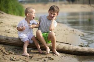 twee broers, de ouderling en de jonger, zijn spelen door de rivier. kinderen Aan de zanderig kust praten en toegeven. foto