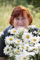 mooi ouderen vrouw met een boeket van madeliefjes glimlachen en op zoek Bij de camera. foto