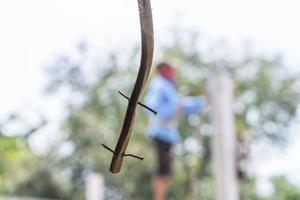 detailopname schot van roestig nagel Aan een houten plank hangende met wazig bouw arbeider staand en groen natuur achtergrond. abstract achtergrond foto