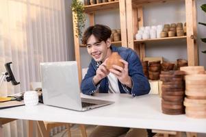 een jong Aziatisch Mens ondernemer leven streaming naar uitverkoop ambacht producten naar klanten in zijn winkel , technologie online bedrijf concept. foto