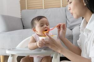 jong moeder helpen baby aan het eten mengsel voedsel Aan baby stoel foto