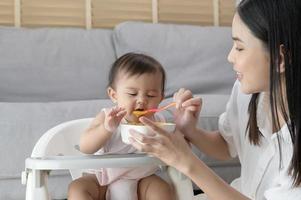 jong moeder helpen baby aan het eten mengsel voedsel Aan baby stoel foto