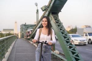 portret van jong mooi vrouw met een elektrisch scooter over- brug in modern stad achtergrond foto