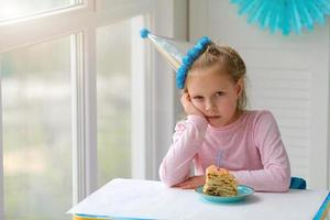 verdrietig weinig meisje zittend in voorkant van een stuk van taart met een kaars. foto