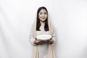 een Aziatisch moslim vrouw is vastend en hongerig en Holding gereedschap bestek terwijl op zoek terzijde denken over wat naar eten foto