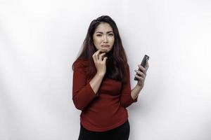 een ontevreden jong Aziatisch vrouw looks ontevreden vervelend rood top geërgerd gezicht uitdrukkingen Holding haar telefoon foto