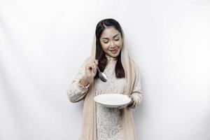 een Aziatisch moslim vrouw is vastend en hongerig en Holding gereedschap bestek terwijl op zoek terzijde denken over wat naar eten foto
