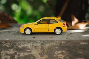 een foto van een geel speelgoed- auto geplaatst in de buurt een boom, na sommige bewerkingen. concept voor natuur avontuur.