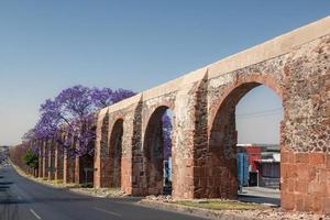 queretaro Mexico aquaduct met jacaranda boom en Purper bloemen foto