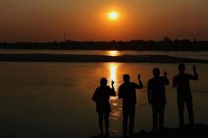silhouet van een groep van mensen maken handen net zo mini hart Bij zonsondergang Aan de rivier- bank. vriendschap concept. foto