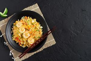 gebakken rijst- met groenten en zee garnalen, wortels, eieren, en tomaten. Thais Chinese voedsel is geregeld Aan een zwart bord Aan een zwart achtergrond keuken tafel, top visie. foto