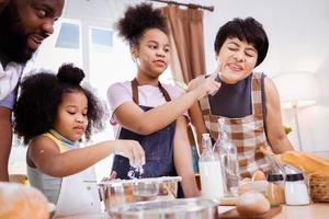 gelukkig Afrikaanse Amerikaans familie genieten samen terwijl bereiden de meel voor maken koekjes Bij huis foto