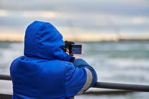 terug visie van Mens toerist nemen foto van zee met smartphone