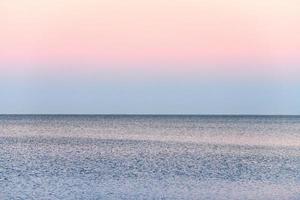 sfeervol romantisch roze rood zee zonsondergang lucht bovenstaand blauw stil water, minimalistisch vredig zeegezicht foto