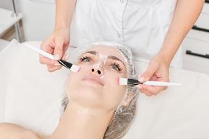 schoonheidsspecialist wrijven room met borstels in vrouw gezicht huid voor verjonging, kunstmatig procedure foto