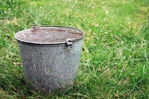 emmer vol van regenwater staand Aan groen gras foto