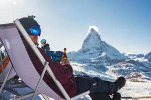 jong snowboarder juichen met een bier na skiën dag in een bar of een cafe Bij de zermatt ski toevlucht in Zwitsers Alpen met een fantastisch visie van de materiehoorn. winter vakantie concept. foto