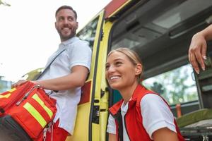 drie paramedici door de ambulance. jong vrouw en Mens lachend. dokter is draag- een medisch trauma tas. foto