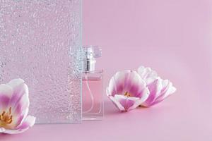 een fles van vrouwen parfum of toilet water staat achter een Verlichting glas Aan een Purper achtergrond met vers voorjaar bloemen. aroma presentatie. foto