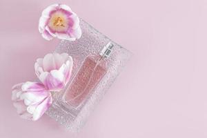 een chique fles van vrouwen parfum leugens Aan een Verlichting glas dienblad met voorjaar tulp bloem hoofden. lila achtergrond. top visie. een kopiëren ruimte. maquette. foto