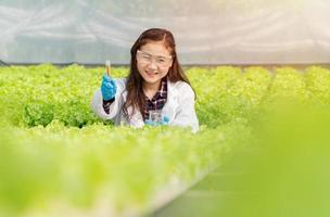 Aziatisch vrouw wetenschappers Holding een Onderzoek buis naar controleren de kwaliteit van water in hydrocultuur boerderij systeem in serre. concept van biologisch voedingsmiddelen controlerend de omgeving, verlichting, temperatuur, water foto