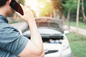 aziatische man met behulp van mobiele telefoon die om hulp vraagt na een autopech op straat. concept van voertuigmotorprobleem of ongeval en noodhulp van professionele monteur foto