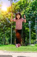 schattig weinig meisje hebben pret Aan een schommel in mooi zomer tuin. kind meisje spelen Aan buitenshuis speelplaats in park. actief zomer vrije tijd voor kinderen foto