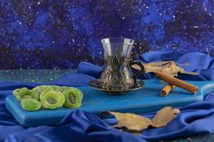 glas thee, kaneelstokjes en gedroogde kiwiplakken op een blauw bord foto