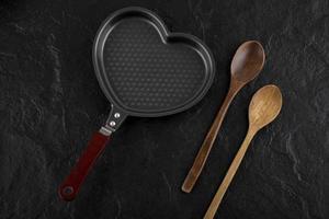 hartvormige pan en een houten lepel op een zwarte achtergrond