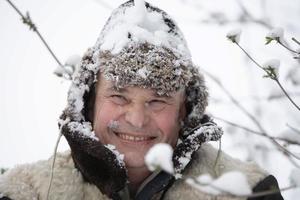 een ouderen Mens in een winter hoed gedekt met sneeuw glimlacht en looks in de camera. foto